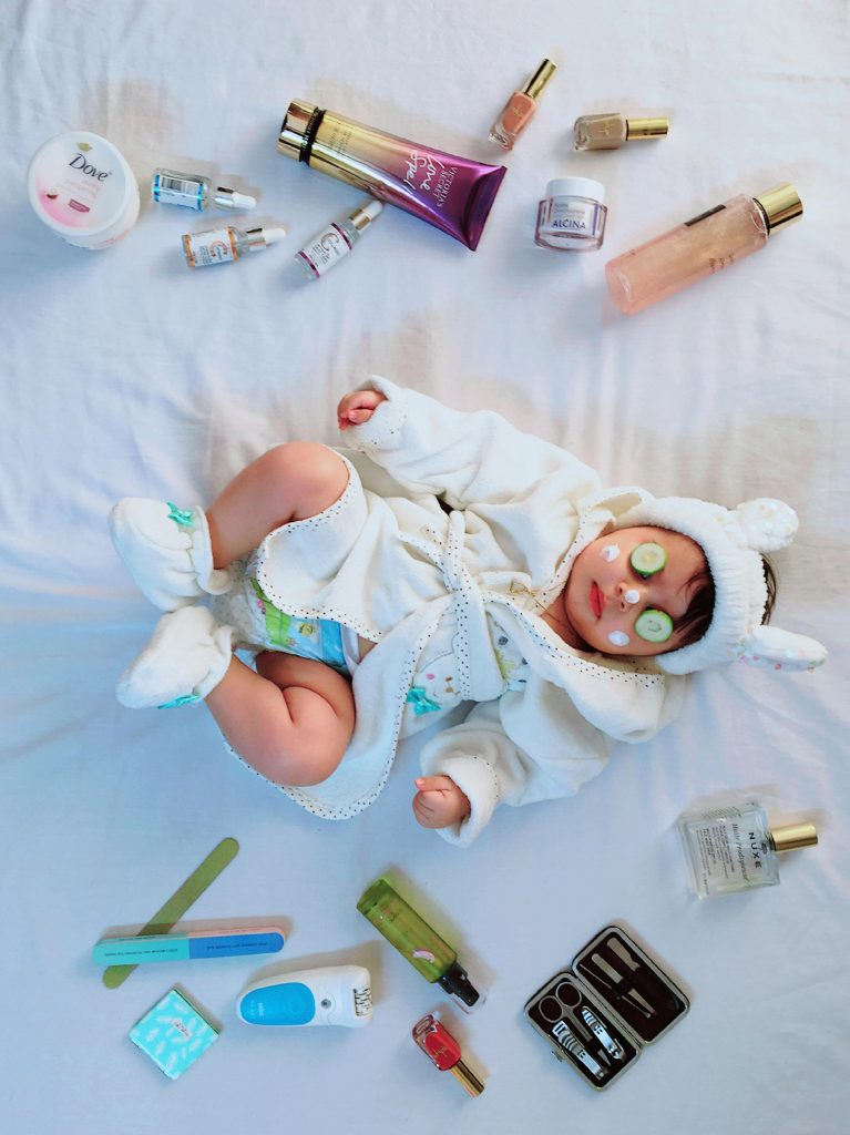 pexels photo 34233828 34233828 Cute baby with cucumber eye mask surrounded by skincare items on a bed.